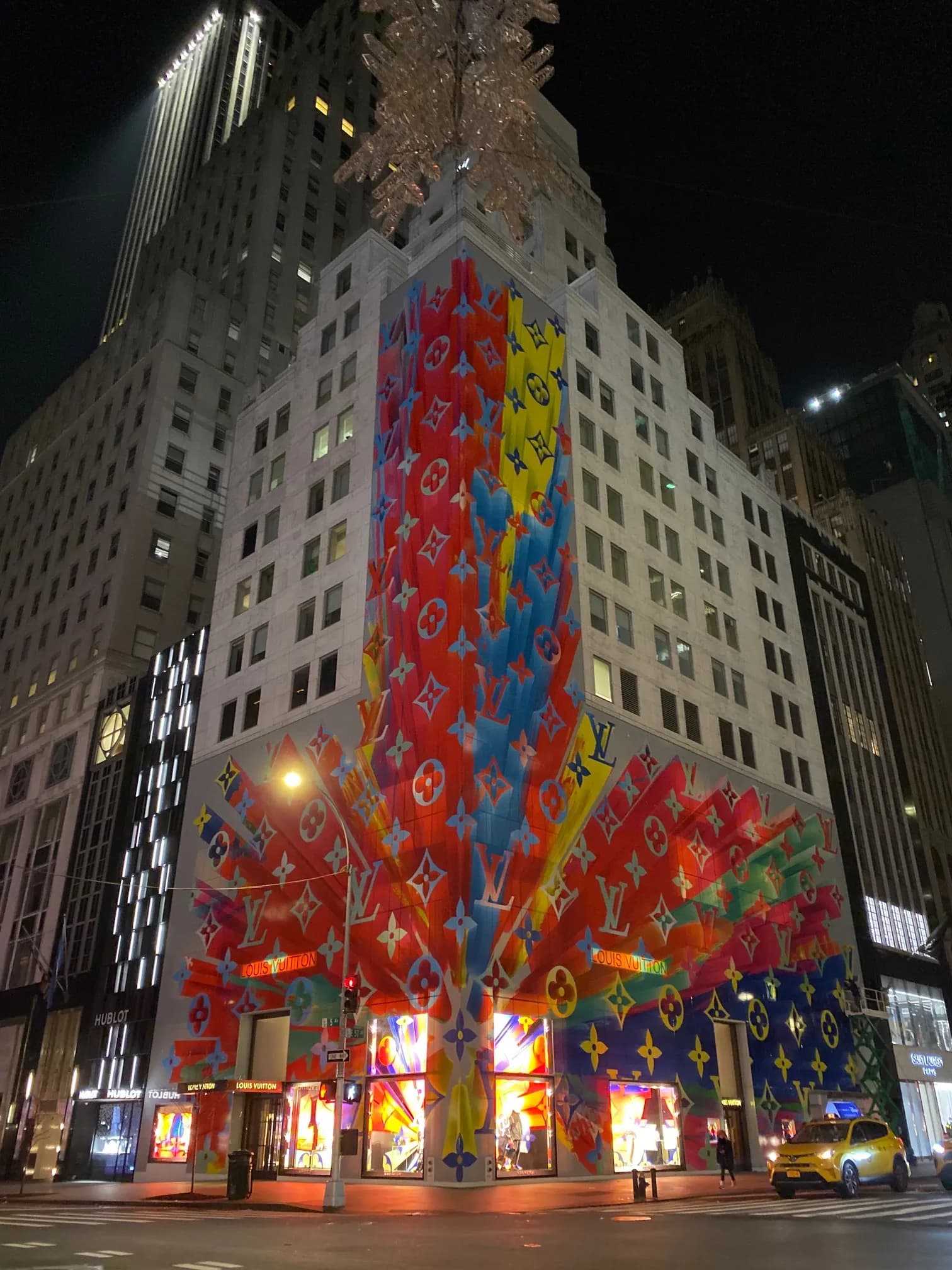 Louis Vuitton tower at night with an explosive multicolor monogram burst climbing the facade