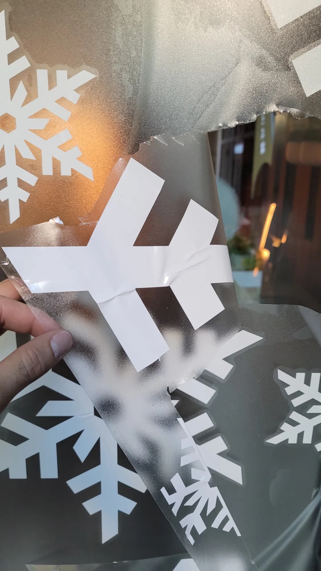 Installer's hand applying a frosted snowflake vinyl decal to storefront glass