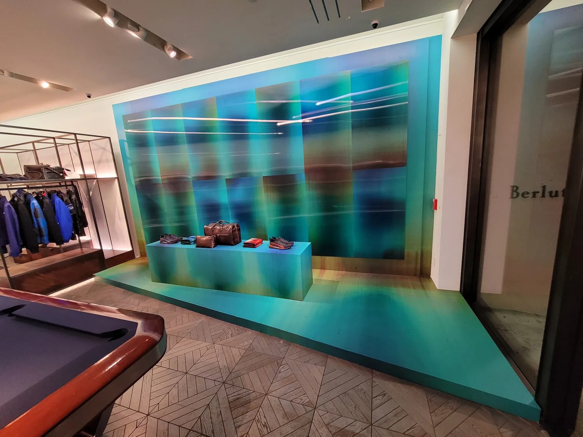 Berluti Miami Design District installation: teal gradient wall and platform displaying leather goods