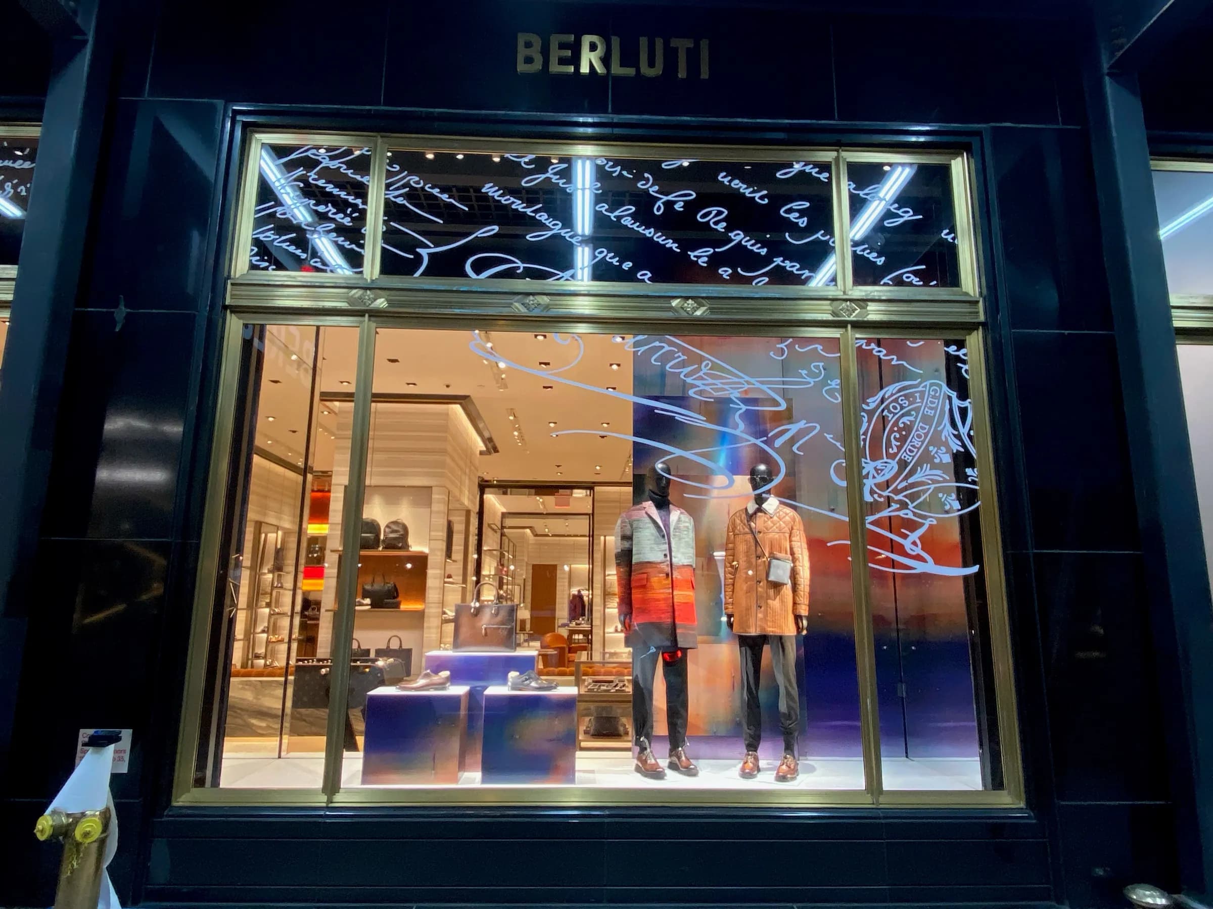 Berluti New York storefront at night with calligraphic script transom graphics and gradient window displays, 2021