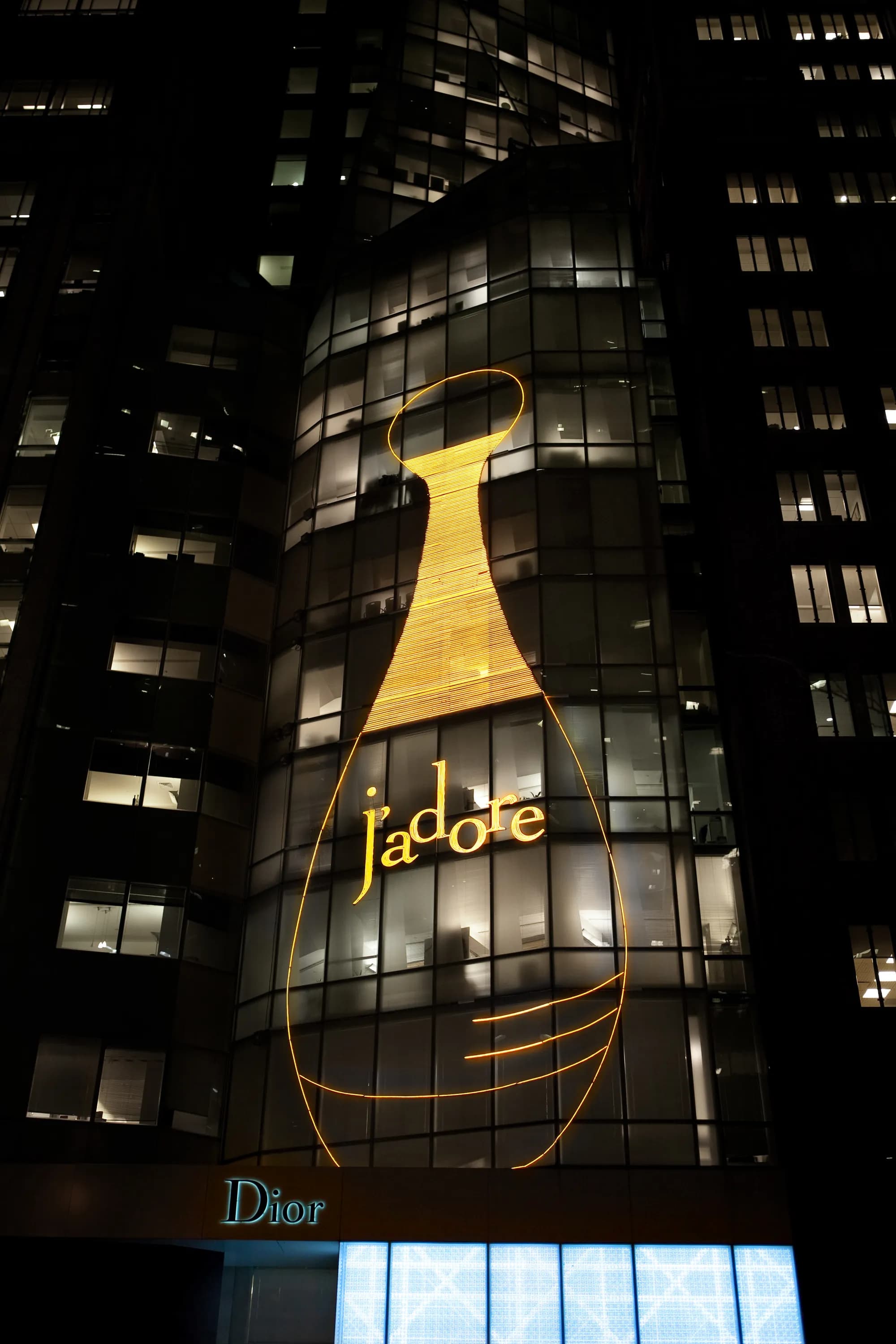 Full-height J'adore bottle drawn in gold light on the Dior 57th Street glass tower, New York