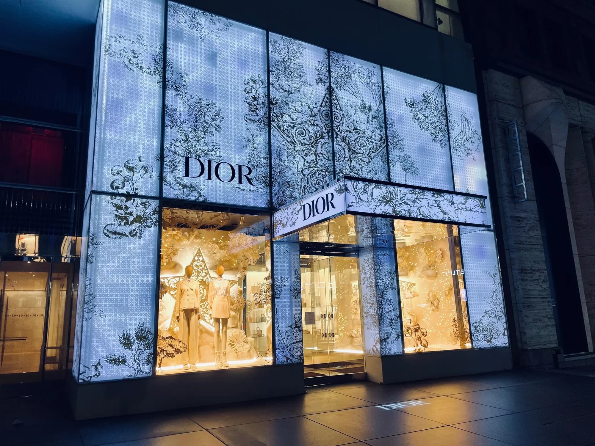 Corner view of the illuminated Dior 57th Street facade with botanical panels and golden windows, 2021