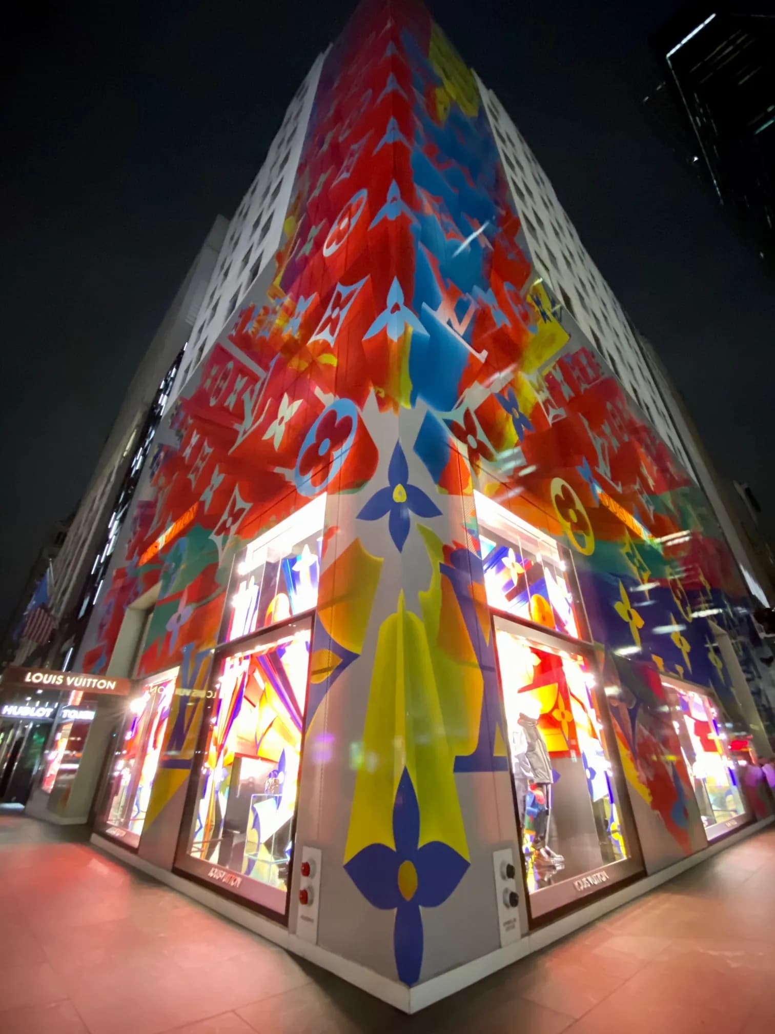 Upward view of the monogram burst facade wrap and illuminated corner windows at night
