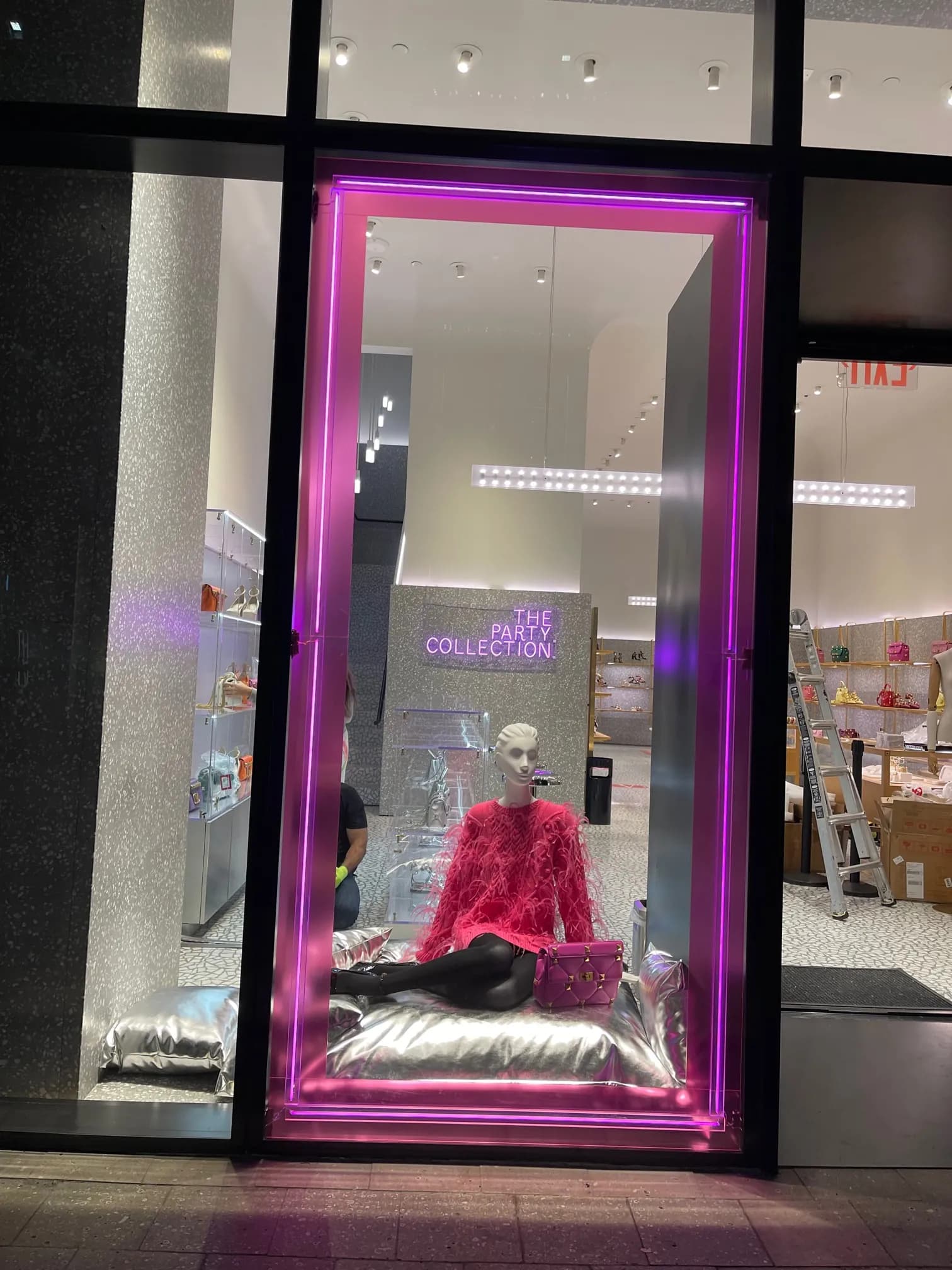 Valentino window framed in magenta neon with a mannequin reclining on silver cushions